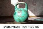 Small photo of A green old Soviet rusty large weight of 16 kilograms stands on the floor of a house on a carpet scratched, worn paint handle, rays of light