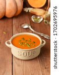 Small photo of Homemade pumpkin quash soup with seeds. Traditional American pumpkin soup in bowl with spoon and ingredients on wooden background. Copy space.