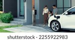 Small photo of Progressive young parents and daughter with electric vehicle and home charging station. Green and clean energy from electric vehicles for healthy environment. Eco power from renewable source at home.