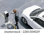 Small photo of Aerial view of progressive businessman in black formal suit with his electric vehicle recharging battery at public car park charging station as vehicle powered by sustainable energy concept.