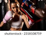 Small photo of Asian female Muay Thai boxer punching in fierce boxing training session, delivering strike to her sparring trainer wearing punching mitts, showcasing Muay Thai boxing technique and skill. Impetus