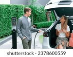 Small photo of Young couple travel with EV electric car charging in green sustainable city outdoor garden in summer shows urban sustainability lifestyle by green clean rechargeable energy of electric vehicle innards