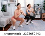Small photo of Vigorous energetic woman with trainer or workout buddy doing exercise at home. Young athletic asian woman strength and endurance training session as home workout routine with squat.