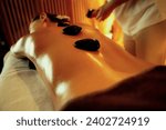 Small photo of Closeup hot stone massage at spa salon in luxury resort with warm candle light, blissful woman customer enjoying spa basalt stone massage glide over body with soothing warmth. Quiescent