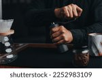 Professional barista making filtered drip coffee in coffee shop. Close up of hands barista grinding coffee beans with hand grinder, pour over coffee with hot water and filter paper in cafe.