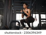Small photo of Strong Asian woman doing exercise with kettlebell at cross fit gym. Athlete female wearing sportswear doing squat workout on grey gym background with weight and dumbbell equipment. Healthy lifestyle.