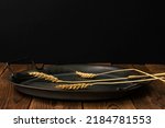 Small photo of Three spikelets of ripe wheat lie on a rustic plate on an old wooden table. Country style. Black background. Meager and poor food. High quality. low key