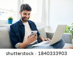 Young man working at home using laptop and smartphone