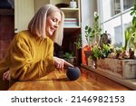 Happy mature woman using smart speaker at home in a kitchen