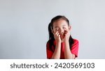 Small photo of portrait of little asian girl tired, lethargic, strain, bored, bad mood concept. studio shot with light color background. pulling funny faces using their hands to pull down on their cheeks distorting