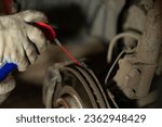 Small photo of A man is repairing a car in a garage. A man treats rusted bolts with WD-40 solution. Replacing a brake disc on a car in the garage. Concept of a man fixing his car in a garage.