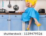 Retro pin up girl woman female housewife wearing colorful top, skirt and white apron holding cooked sweet strawberry milkshake sitting in the kitchen with utensils and tray with cupcakes.
