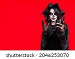 Woman in Halloween costume wear lace gloves, with creative sugar skull makeup in black witch hat. Do spell on wide isolated red background. Ð¡oncept Los Muertos poster party or La Calavera Catrina. 