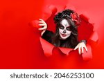 Girl with creative sugar skull makeup with wreath of flowers on head, wide isolated red paper hole background. Holiday concept Dia De Los Muertos  on poster for Halloween party or La Calavera Catrina
