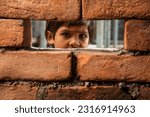 Small photo of An Indian labour girl child looking through under construction brick wall window