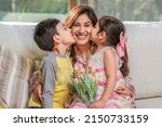 Small photo of Mother's Day. Latin mother holds her two children, a boy, and a girl, as they hug and kiss her.