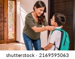 Beautiful loving  Latin mother with her children at the door of her house. Mother greets her children who return from school. Children with uniforms and backpacks.