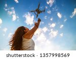 Back view of woman standing on the beach with raised hands holding drone over beautiful sea and summer blue sky background.