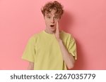 Small photo of Studio shot of dazed impressed surprised curly-haired man learned shocking rumor standing with dropped jaw and wide eyes looking at camera touching cheek with hand isolated over pink background.