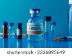 Small photo of closeup of a simulated vial of fentanyl on a blue table next to a syringe and some other different vials