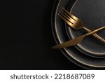 Small photo of The golden tableware is placed on a ceramic dinner plate. The background is black leather. Luxurious, sumptuous fine tableware.Flat lay, top view, banner,horizontal photo