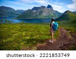 backpacker girl hiking hesten trailhead overlooking the town of fjordgard and mighty mountains in norway, senja island hiking, famous segla mountain