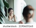 Small photo of A young Asian woman talks to herself through a mirror to build her self-confidence and empower herself.