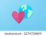 Globe and red heart shape made from paper isolated on blue background. Save the wold, Global healthcare and Green Earth day concept.
