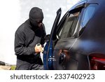 Small photo of A criminal man with open the door and break into the car. He uses a screwdriver. Hijacker, the concept of car theft