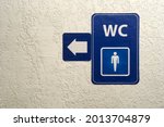 Arrow, pointer on blue plate of public male toilet signÐ± on plastered wall. Toilet sign. Restroom Concept .WC. Horizontal shot. Copy space. Close-up. Indoors.