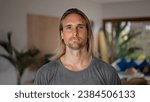 Small photo of Happy male person face home portrait. Blue eyes look at camera close up. Joyful bristle surfer man long hair. Smiling shy guy. Kind people portraits. Young adult hippie inside house. Hipster hairstyle