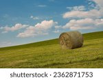 Small photo of Background with bale of straw on mown meadow with blue sky and clouds. A bale of straw on a meadow in the light of the setting sun.
