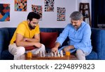 Small photo of A middle-aged son and an elderly old man playing a game of chess together - quality family time, father-son bonding . An attractive male in his thirties concentrating while playing a board game wit...
