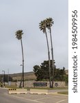 Small photo of Lompoc, CA, USA - May 26, 2021: Portrait, Vandenberg Space Force Base entrance seen from street with emblem, palm trees and plants, yellow road barriers, under gray sky.