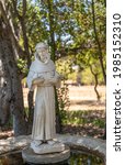 Small photo of Santa Inez, CA, USA - May 26, 2021: San Lorenzo Seminary. White Saint Francis statue in garden fountain under shadow of trees. Hold 2 birds.