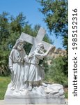 Small photo of Santa Inez, CA, USA - April 3, 2009: San Lorenzo Seminary. Station of the Cross number 5 white marble statue. Simon of Cyrene helps Jesus. Under blue sky with green foliage in back.