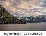 Small photo of Disenchantment Bay, Alaska, USA - July 21, 2011: Wide view on northern port under blue cloudscape. Green forested mountain flank over gray ocean water. Snow covered mountain range on horizon. Glacier