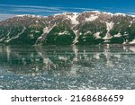Small photo of Disenchantment Bay, Alaska, USA - July 21, 2011: Floating ice pieces on ocean water in front of snow topped mountain range with 4 short glaciers unde blue cloudscape. Forested shoreline.