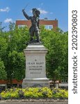 Small photo of Europe, France, Dunkerque - July 9, 2022: Closeup of Jean Bart statue on square named after him, on pedestal with green foliage in back, under blue sky, and yellow flowers at bottom