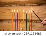 Small photo of A woman's hand with a shamash candle lights the Hanukkah candles at the table. Horizontal photo.