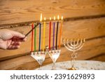 Small photo of A woman's hand with a shamash candle lights the Hanukkah candles at the table. Horizontal photo.