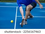 Small photo of Male pickleball player digs deep to scoop up the ball off the co