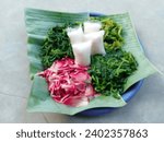 Small photo of pecel or traditional Indonesian food contains boiled torch ginger, boiled spinach, boiled kenikir plant (cosmos caudatus), boiled water spinach and rice cake. vegetable salad. defocused