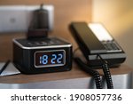 Blurred image of digital alarm clock at hotel room sitting on bedside table along with the telephone. Time management concept. 
