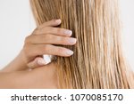 Young woman with hand touching her wet, blonde, perfect hair after shower on the gray background. Care about beautiful, healthy and clean hair. Beauty salon concept. Back view.