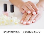Young, perfect, groomed woman's hands with pink and white nail varnish bottles. Nails care. Manicure, pedicure beauty salon. Beautiful jasmine blossoms on table. Fresh flowers.
