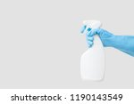 Cleaner's hand in blue rubber protective glove holding a white chemical spray bottle. Empty place for text or logo on gray background. Early spring or regular cleanup. Commercial cleaning company.