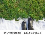 Welcome spring. Goodbye winter. Black woman boots standing on white melting  snow. Empty place for text, quote or sayings on green grass. Point of view shot. Closeup. 