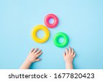 Baby hands playing with green, yellow and pink plastic rings on light blue table background. Pastel color. Closeup. Toys of development for little kids.