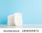 Stack of white soft new baby diapers on wooden table at light blue wall background. Pastel color. Closeup. Empty place for text or logo.